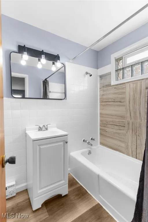 Bathroom with wood finished floors, vanity, tile walls, and shower / bath combo