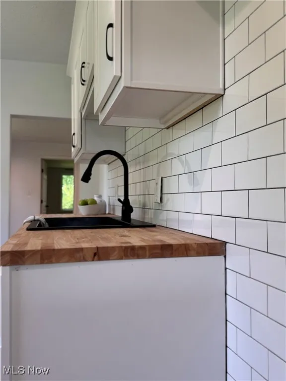 Kitchen view of wood counters, white cabinetry, backsplash, and a peninsula