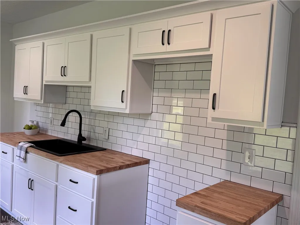 Kitchen with wood counters, backsplash, and white cabinets