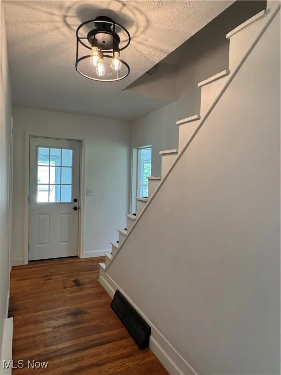 Foyer entrance with stairs, a textured ceiling, and dark wood-style flooring