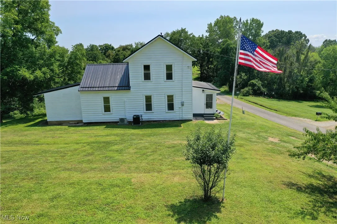 View of side of property with a metal roof, a yard, entry steps, and view of scattered trees