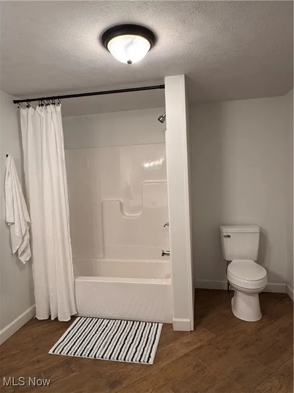 Bathroom with a textured ceiling, shower / bath combo with shower curtain, and tile finished floors