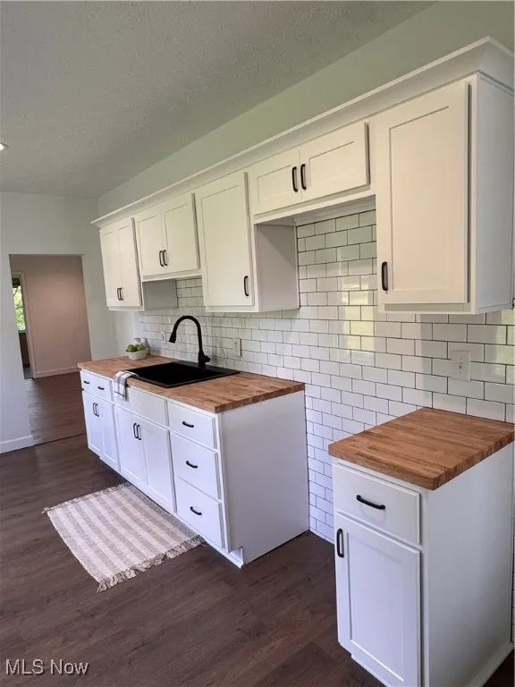 Kitchen with butcher block countertops, dark wood finished floors, decorative backsplash, white cabinets, and a textured ceiling