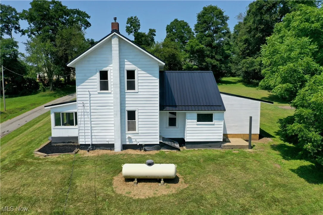 Rear view of house featuring a yard, a metal roof, a chimney, a standing seam roof, and view of scattered trees