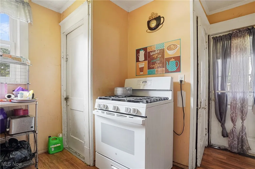 Kitchen with white gas stove, wood finished floors, and ornamental molding