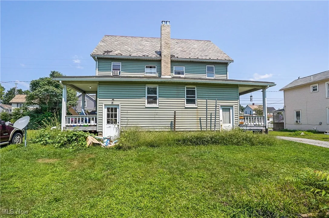 Rear view of property with a yard, a high end roof, a chimney, and covered porch