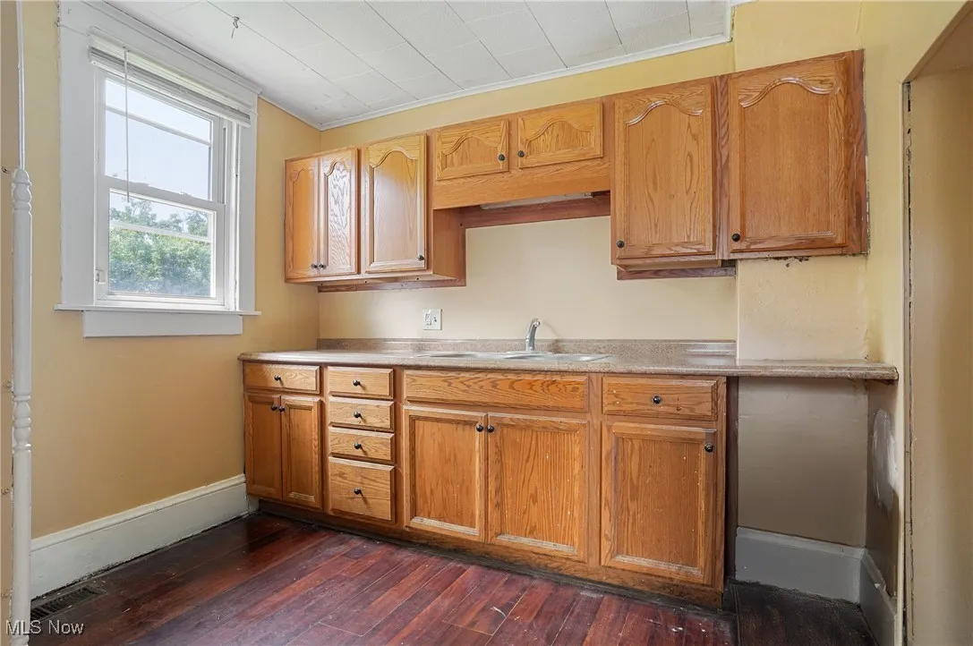Kitchen featuring dark wood-style floors, light countertops, brown cabinetry, and ornamental molding