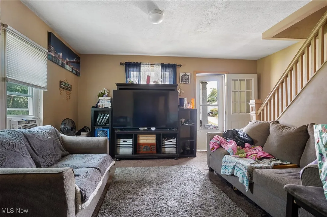 Living room with carpet flooring, a textured ceiling, and stairs