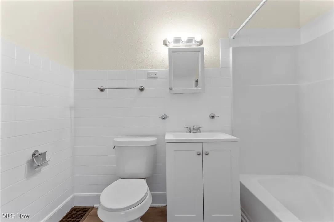 Full bath featuring a textured wall, vanity, tile walls, bathing tub / shower combination, and a wainscoted wall