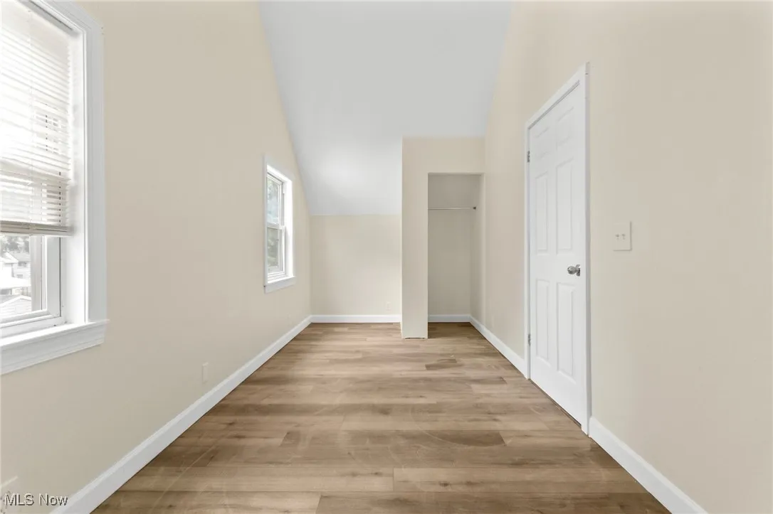Corridor with vaulted ceiling and light wood-type flooring