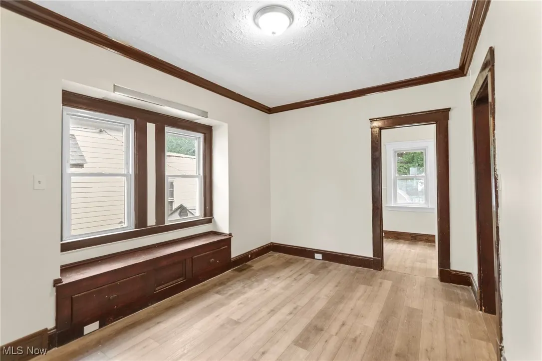Spare room featuring light wood-style floors, a textured ceiling, and crown molding