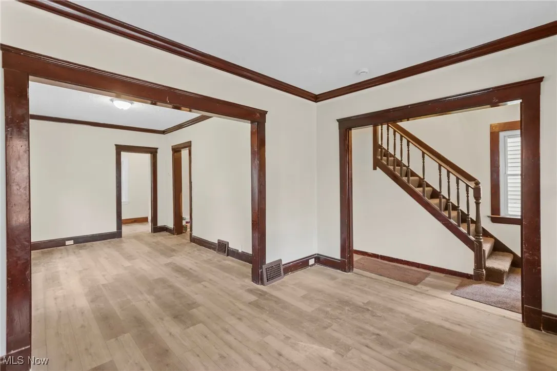 Unfurnished living room featuring crown molding, stairs, and wood finished floors