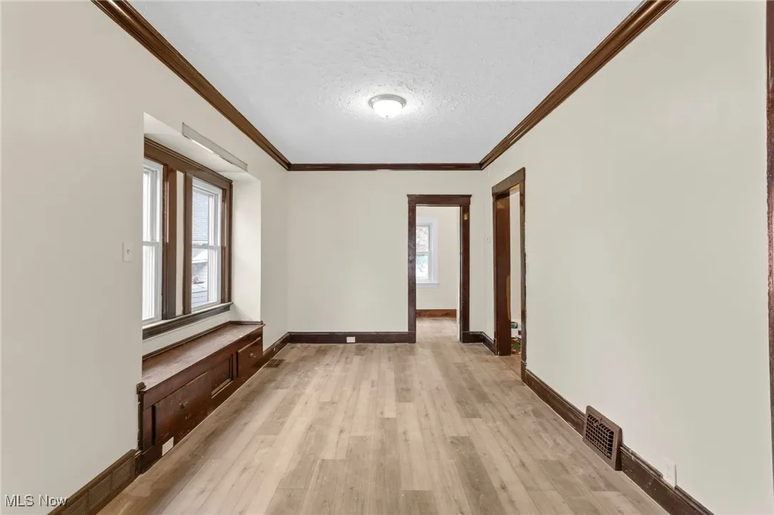 Hallway with crown molding, light wood finished floors, healthy amount of natural light, and a textured ceiling