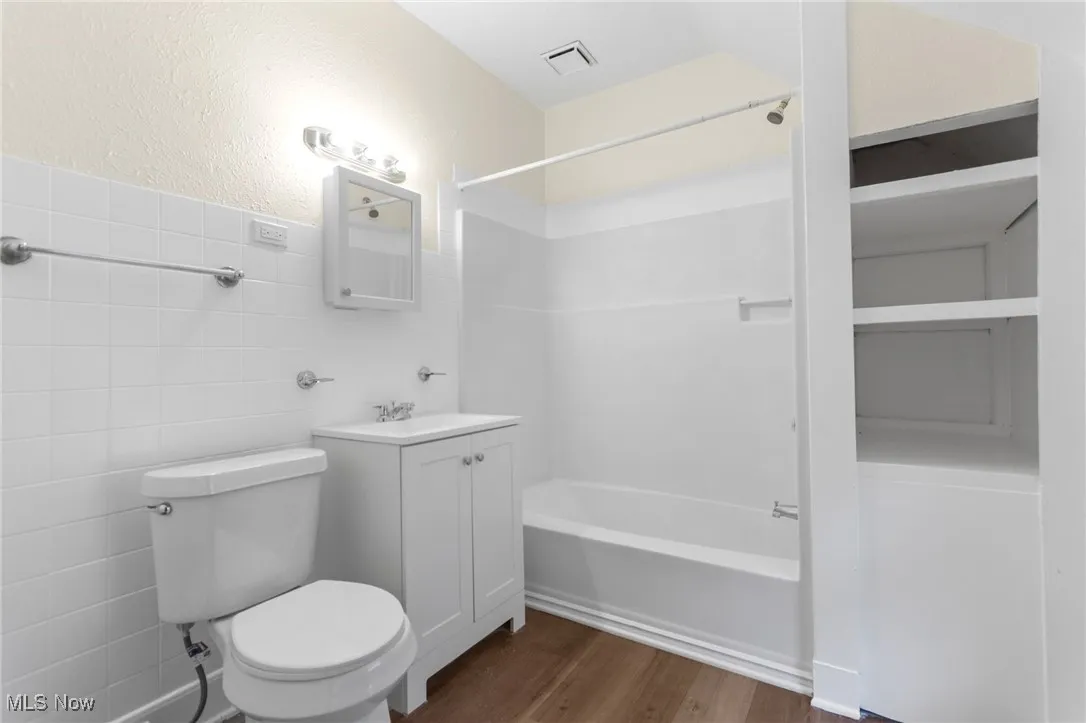 Bathroom with washtub / shower combination, wood finished floors, tile walls, vanity, and a textured wall