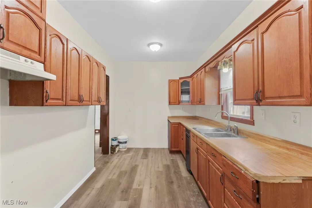 Kitchen featuring light wood-type flooring, light countertops, brown cabinetry, and under cabinet range hood
