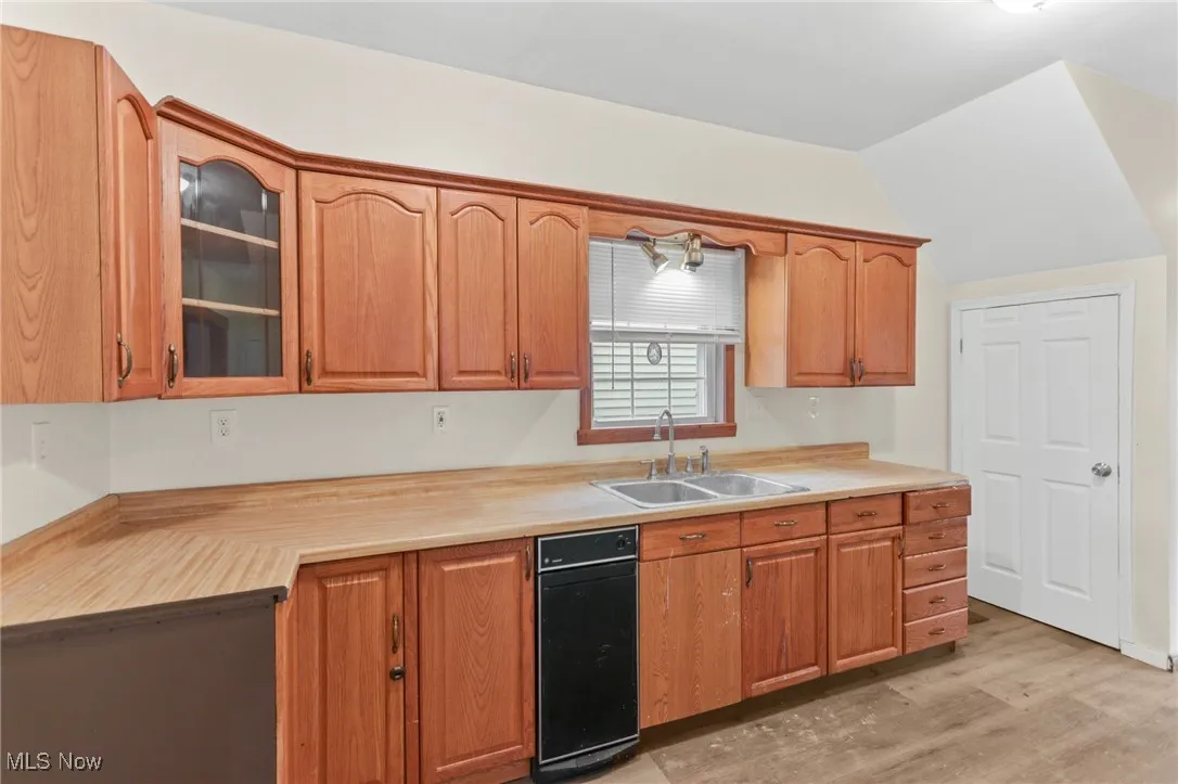 Kitchen with glass insert cabinets, light wood-type flooring, light countertops, lofted ceiling, and brown cabinetry