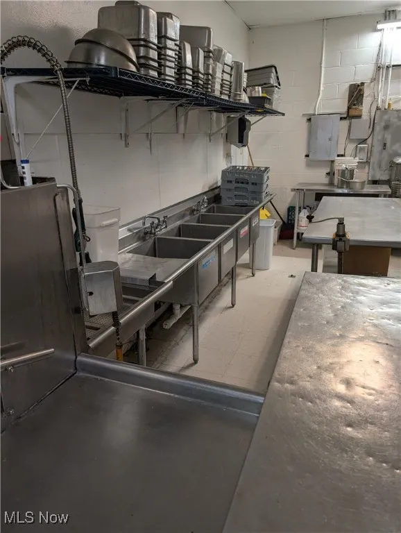 Kitchen with concrete block wall, open shelves, electric panel, and concrete flooring