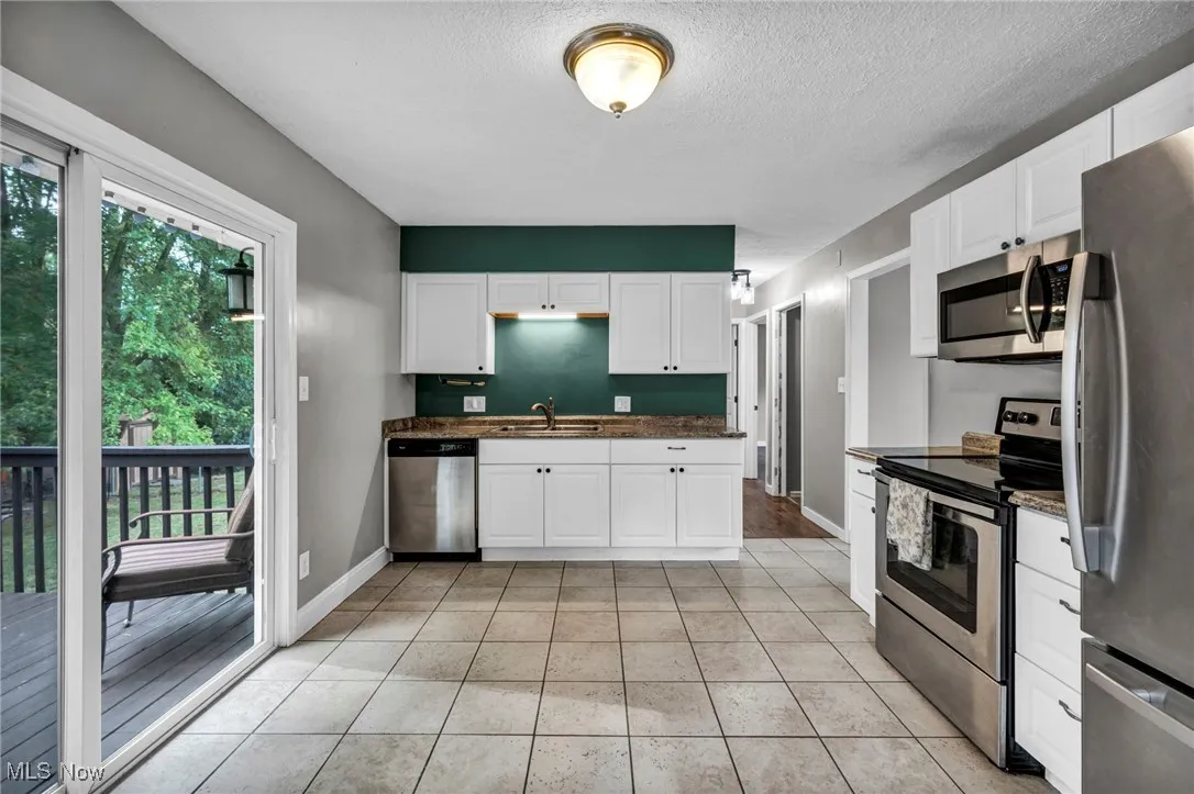 Kitchen with appliances with stainless steel finishes, dark countertops, a textured ceiling, white cabinets, and light tile patterned floors