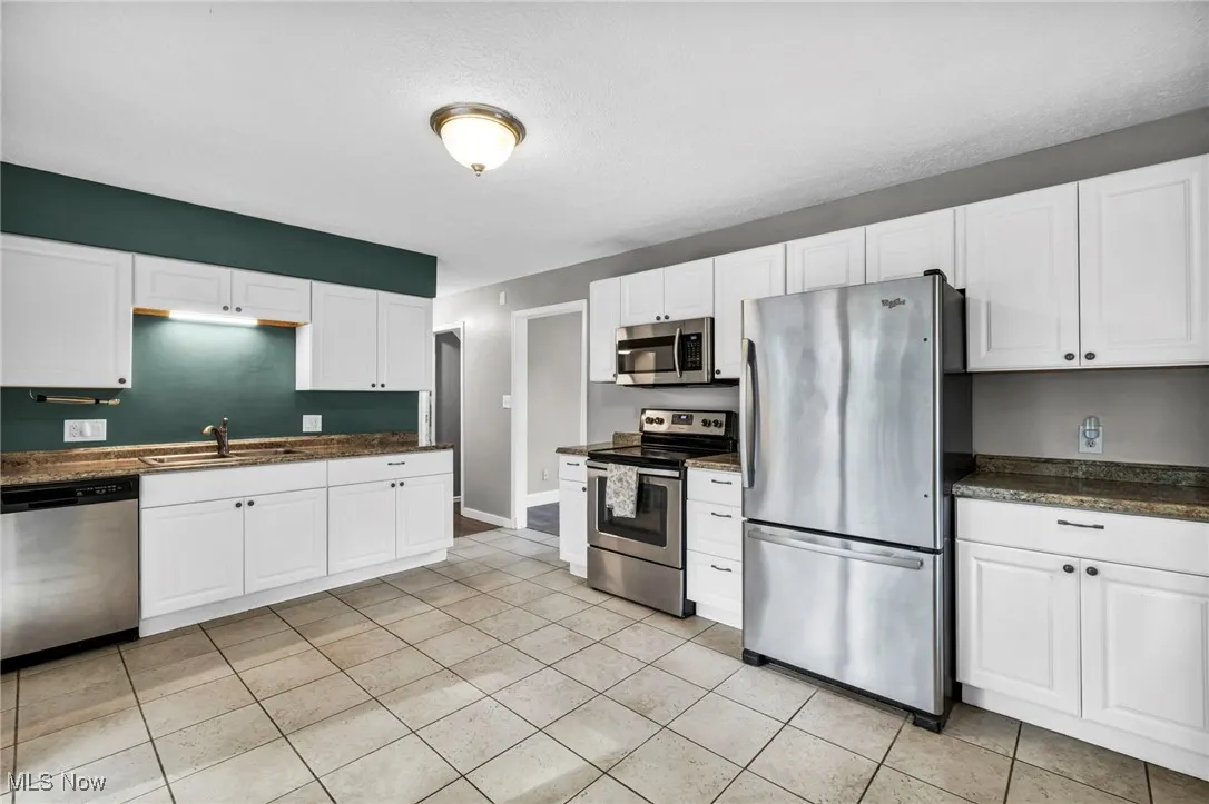 Kitchen with appliances with stainless steel finishes, dark countertops, white cabinets, light tile patterned flooring, and a textured ceiling