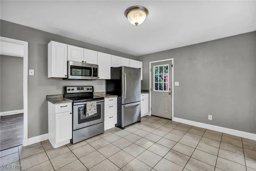Kitchen with stainless steel appliances, white cabinets, light tile patterned floors, dark stone countertops, and a textured ceiling
