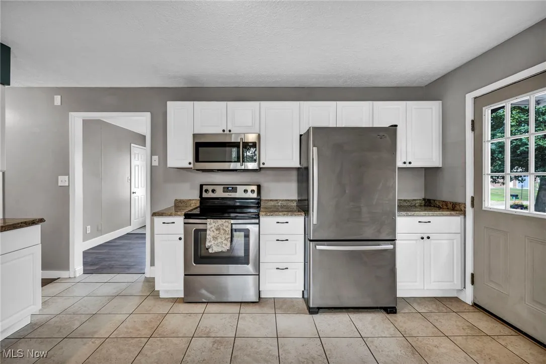 Kitchen featuring stainless steel appliances, white cabinets, a textured ceiling, light tile patterned flooring, and dark stone counters