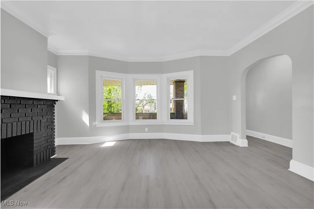 Unfurnished living room with arched walkways, ornamental molding, wood finished floors, and a fireplace