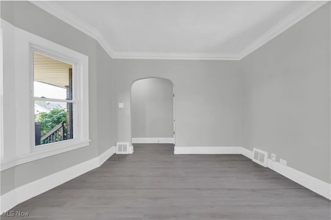 Unfurnished room featuring arched walkways, crown molding, and wood finished floors