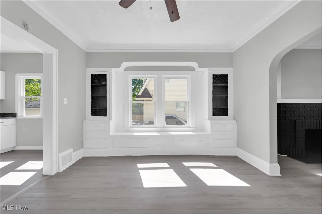 Unfurnished room with plenty of natural light, wood finished floors, crown molding, arched walkways, and a textured ceiling
