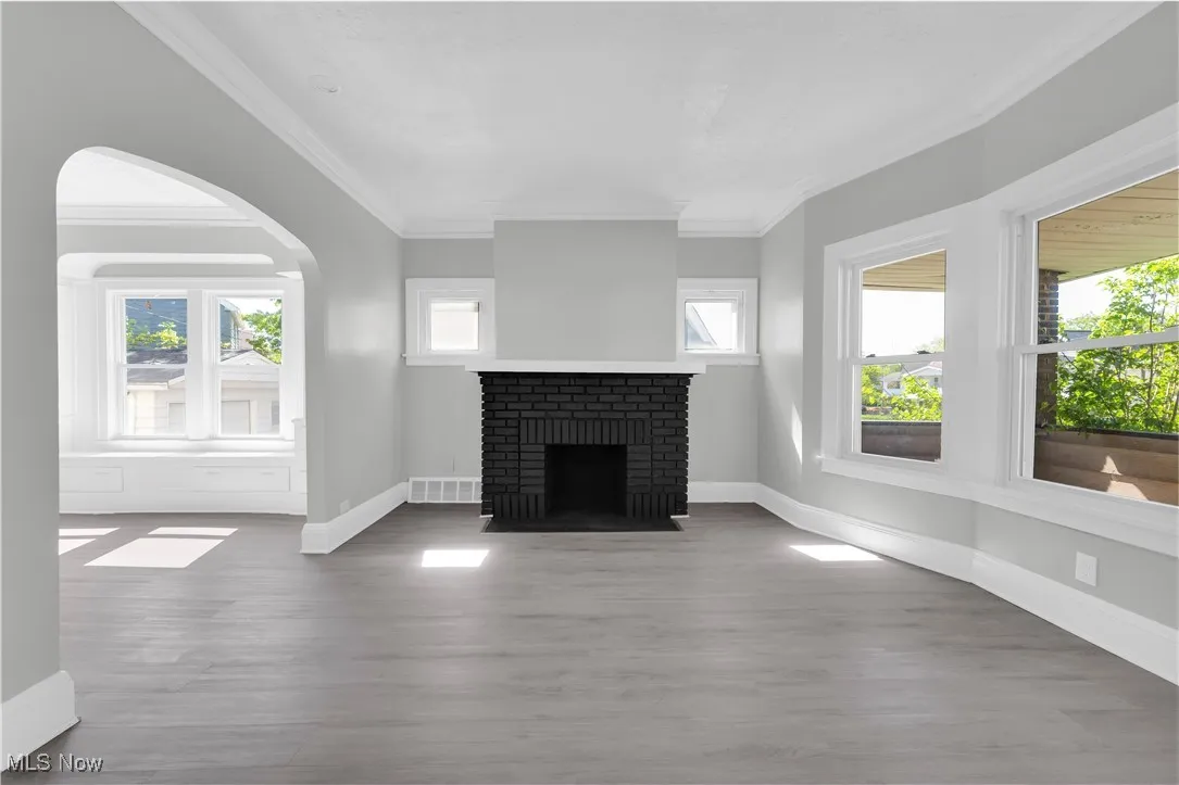 Unfurnished living room with arched walkways, wood finished floors, a fireplace, and ornamental molding