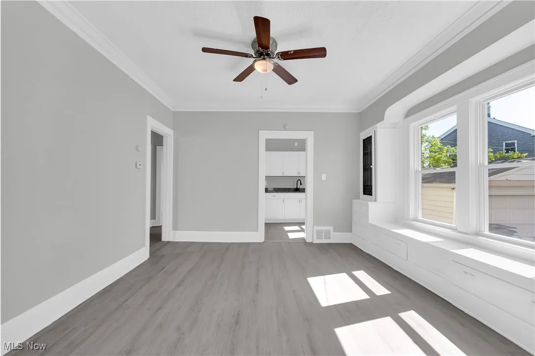 Unfurnished living room featuring crown molding, light wood-type flooring, and ceiling fan