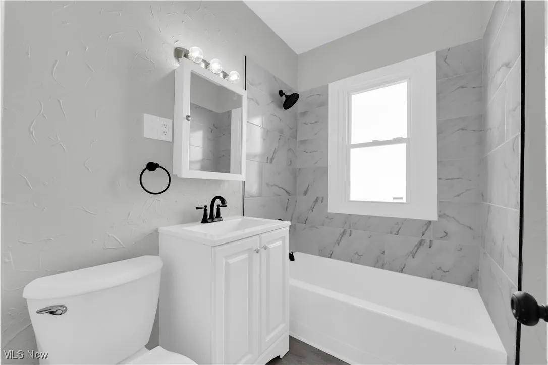Bathroom with a textured wall, vanity, and shower / bathtub combination