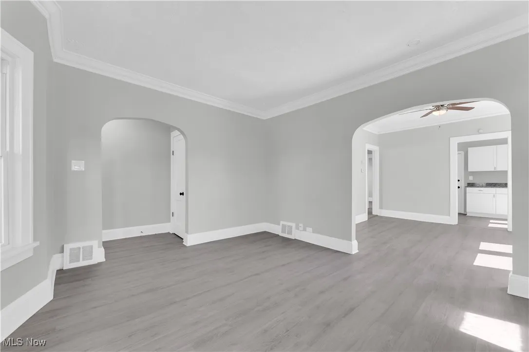Unfurnished room featuring crown molding, wood finished floors, arched walkways, and ceiling fan