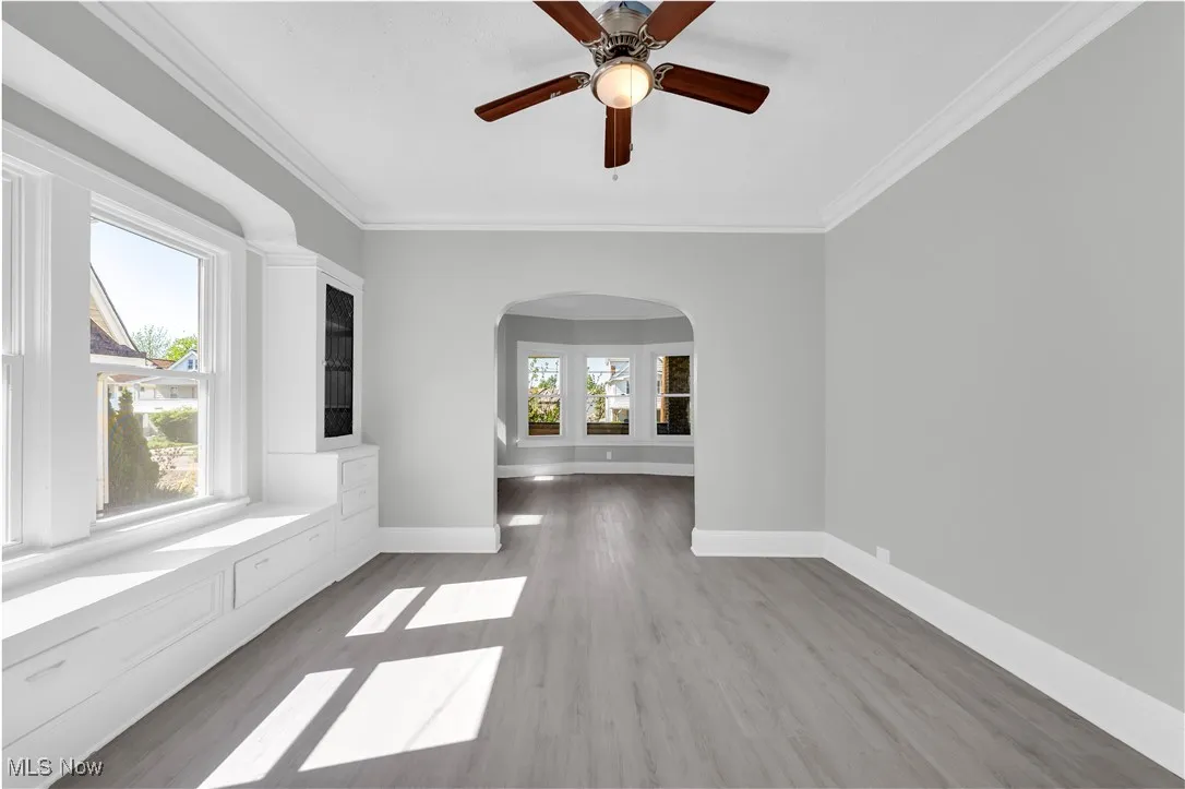 Empty room featuring wood finished floors, ornamental molding, arched walkways, and ceiling fan
