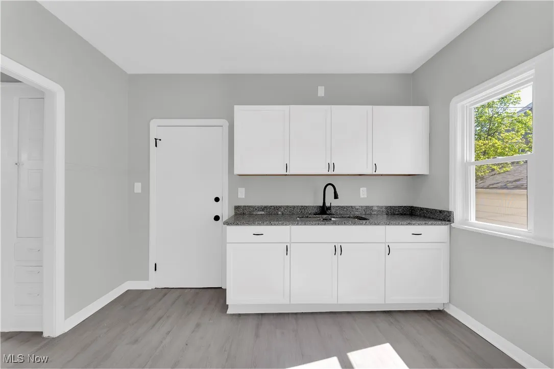 Kitchen with white cabinets, light wood finished floors, and dark stone countertops