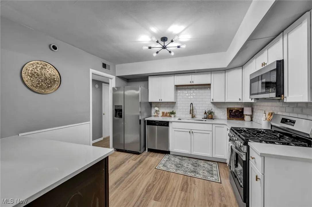 Kitchen with appliances with stainless steel finishes, backsplash, light wood-type flooring, light countertops, and a chandelier