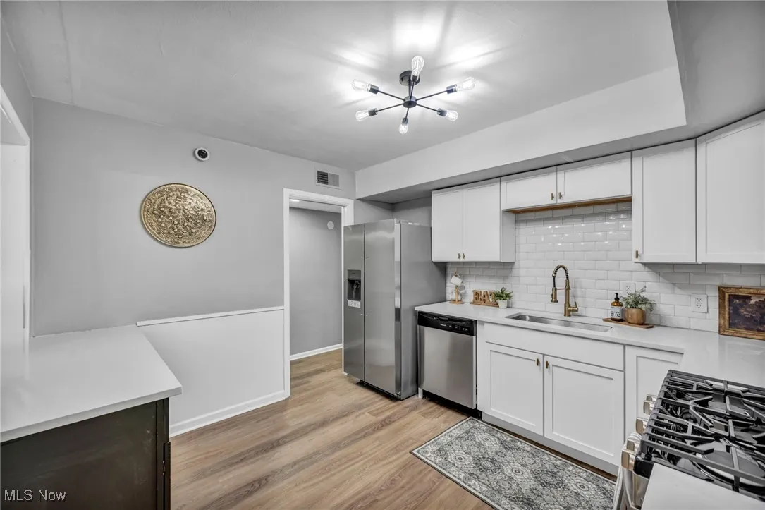 Kitchen with range with gas cooktop, decorative backsplash, light countertops, light wood-type flooring, and white cabinetry