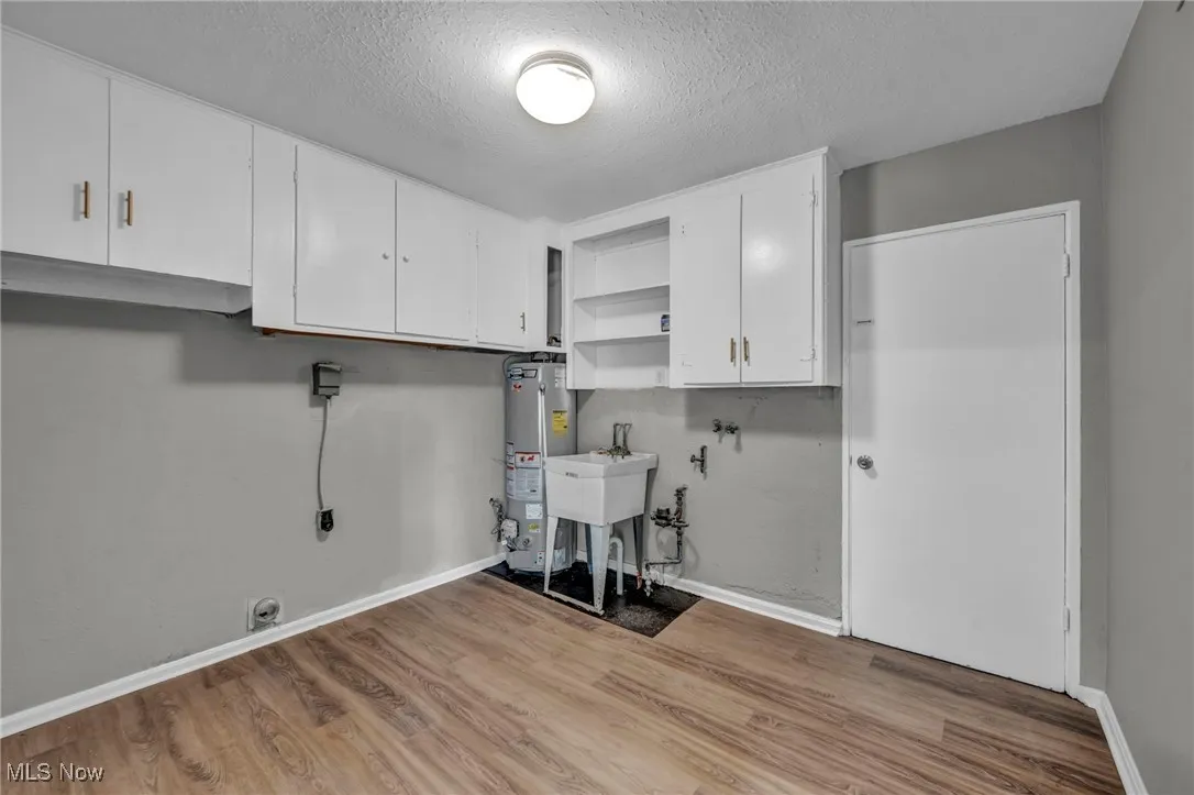 Laundry room featuring cabinet space, a textured ceiling, electric dryer hookup, light wood-type flooring, and water heater