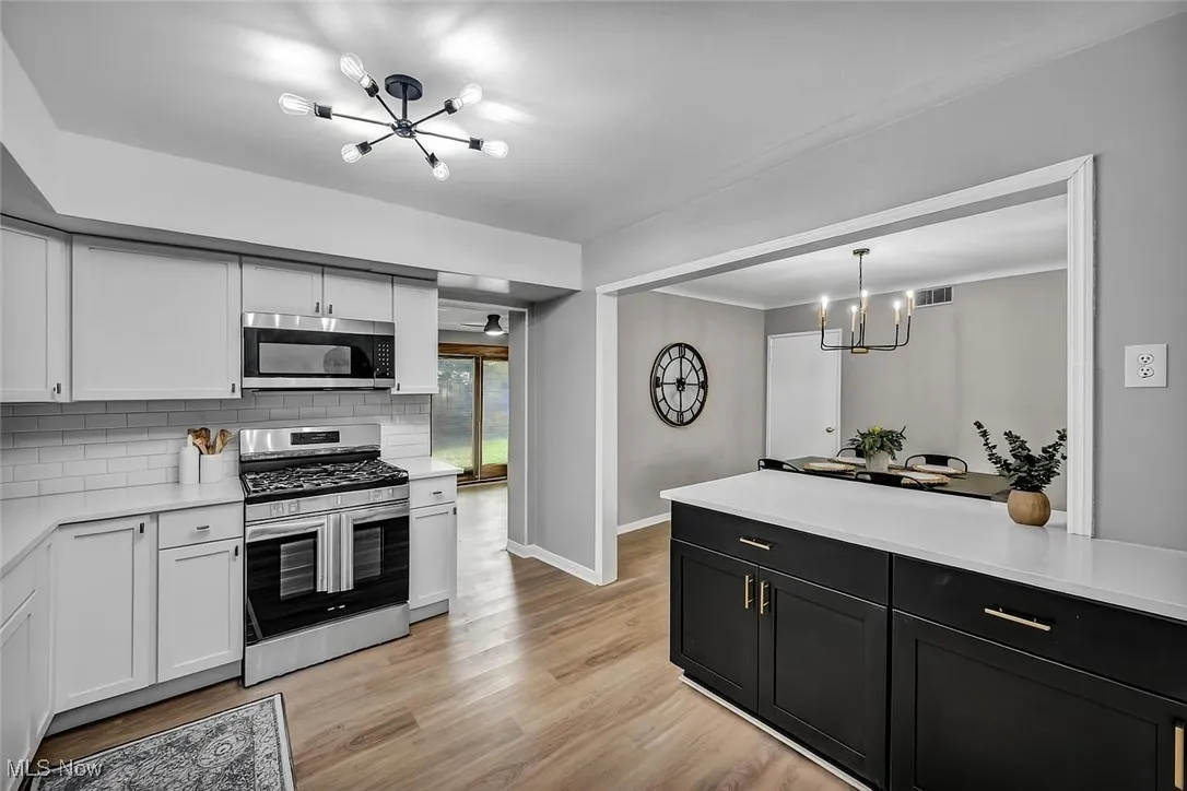 Kitchen with a chandelier, appliances with stainless steel finishes, light wood-style flooring, light countertops, and crown molding