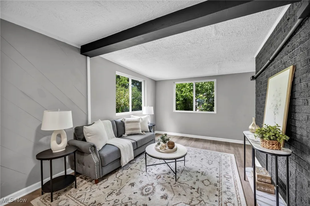 Living room with a textured ceiling, wood finished floors, and beam ceiling