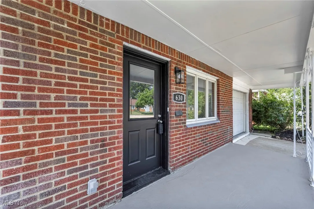 Property entrance with brick siding, a porch, and a garage