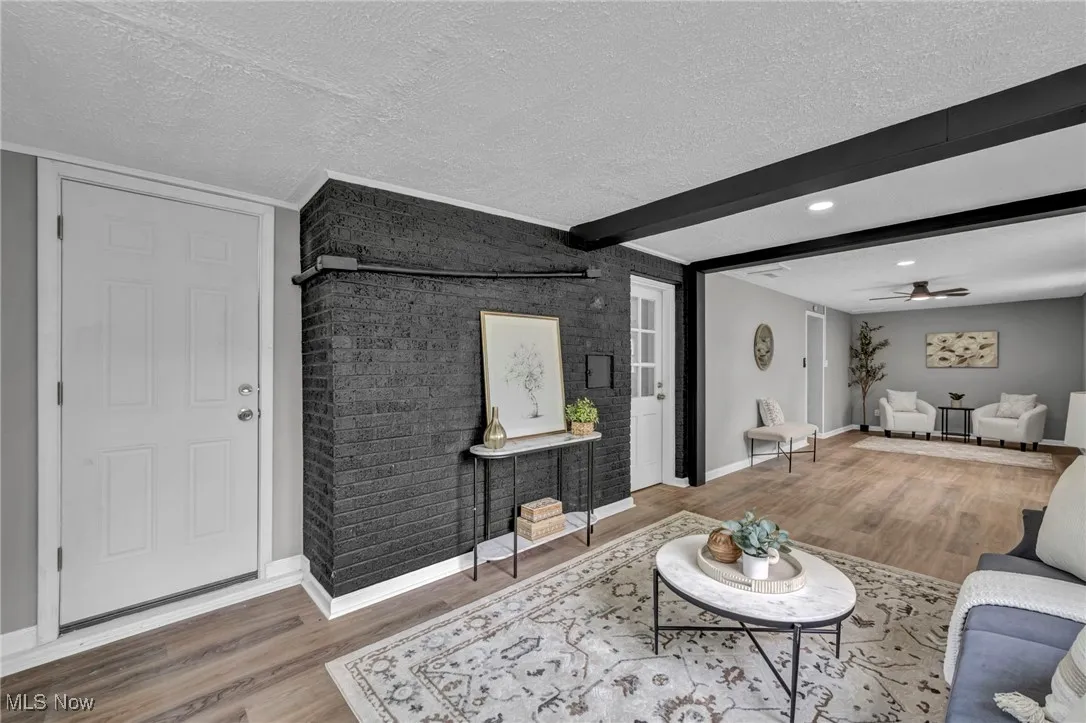 Living area with wood finished floors, ceiling fan, brick wall, beam ceiling, and a textured ceiling