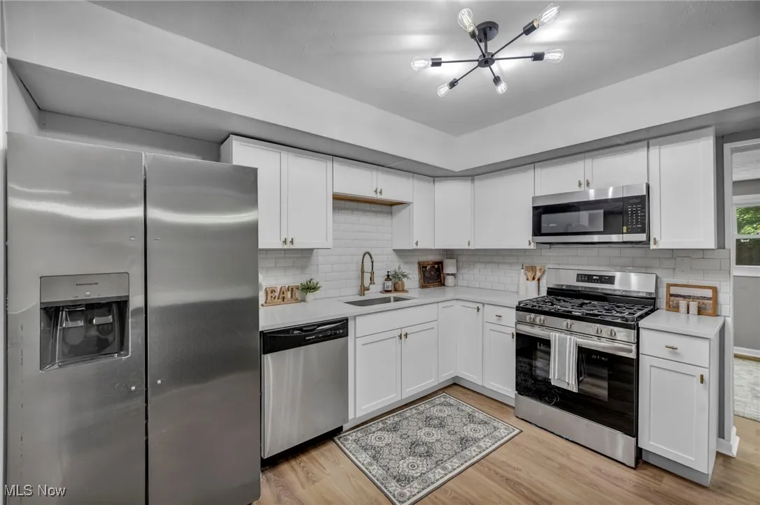 Kitchen with stainless steel appliances, light countertops, white cabinets, light wood-type flooring, and decorative backsplash
