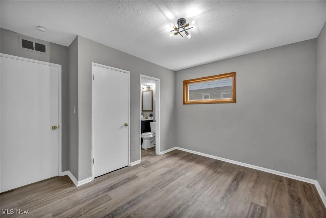 Unfurnished bedroom featuring wood finished floors, a textured ceiling, and ensuite bath