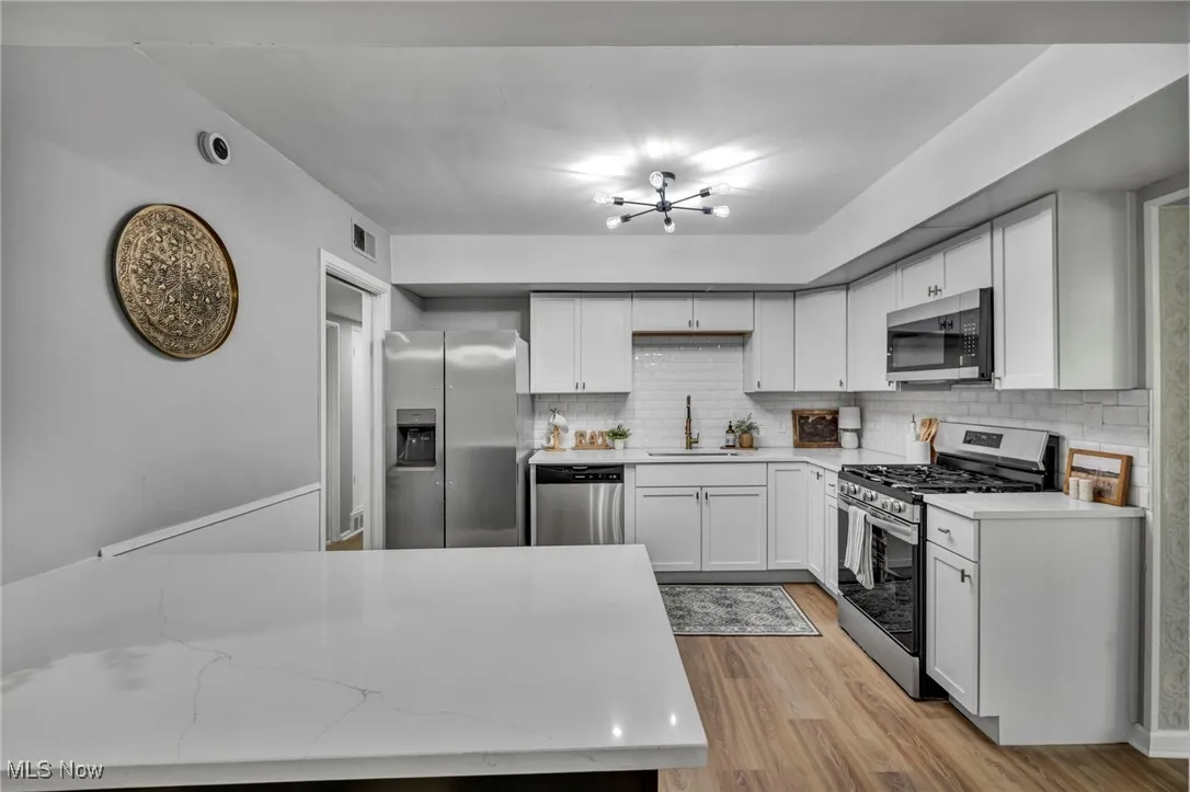 Kitchen with stainless steel appliances, backsplash, light wood finished floors, a chandelier, and white cabinets