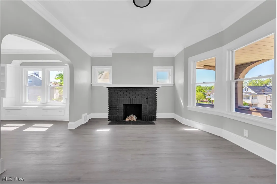 Unfurnished living room featuring ornamental molding, a brick fireplace, wood finished floors, and arched walkways