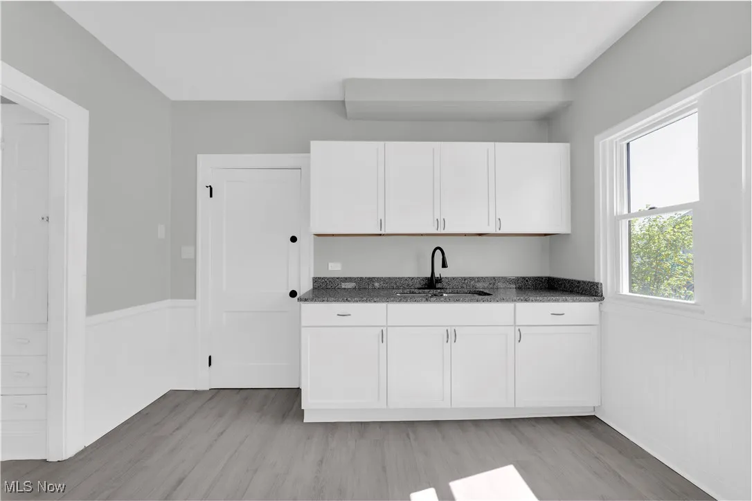 Kitchen featuring a wainscoted wall, white cabinets, light wood-type flooring, and dark stone counters