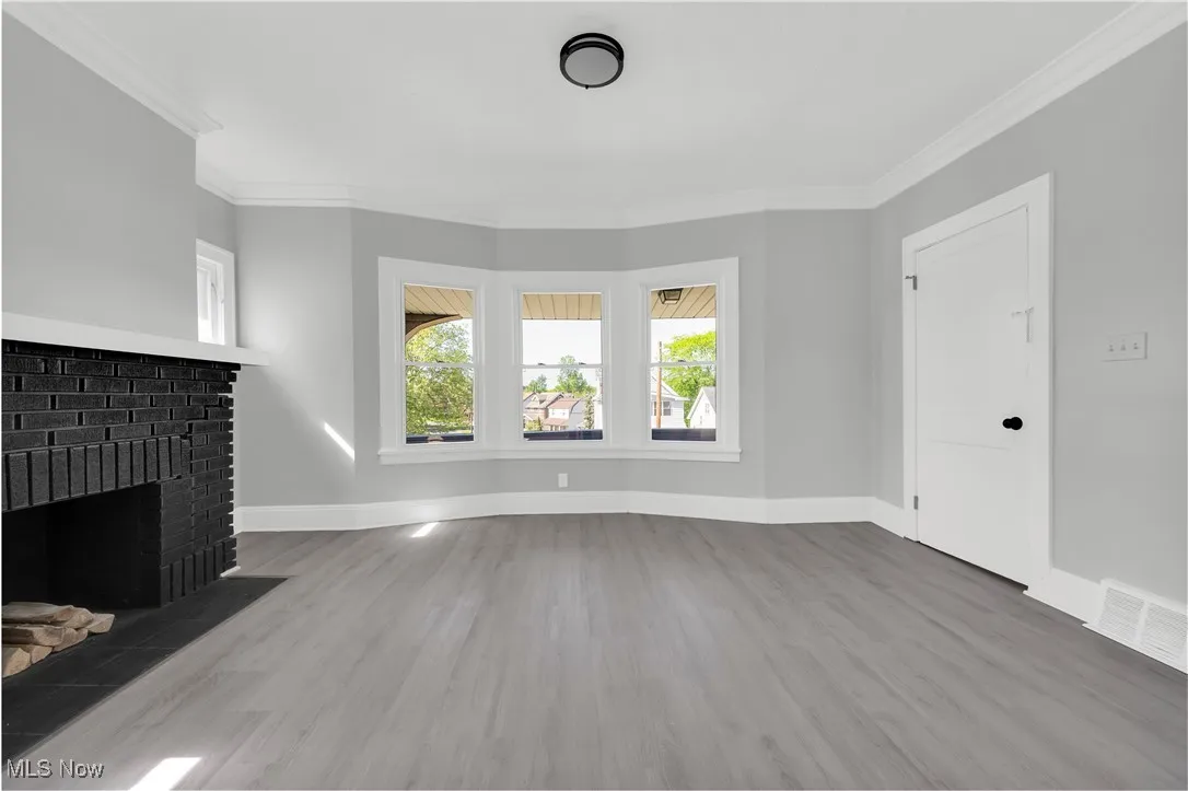 Unfurnished living room featuring ornamental molding, wood finished floors, and a fireplace