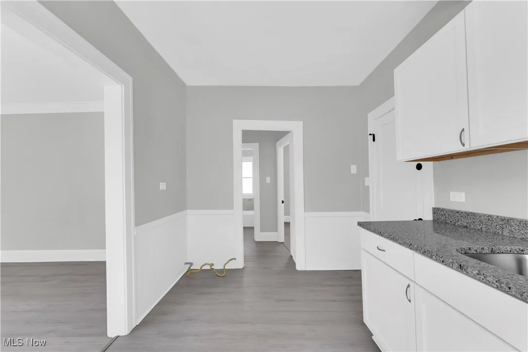 Kitchen featuring dark stone countertops, light wood finished floors, white cabinetry, and wainscoting