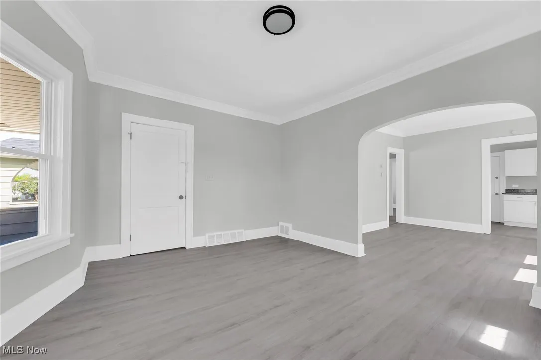 Spare room with crown molding, wood finished floors, and arched walkways