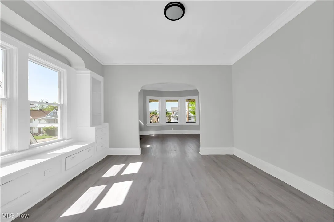 Empty room featuring wood finished floors, crown molding, and arched walkways